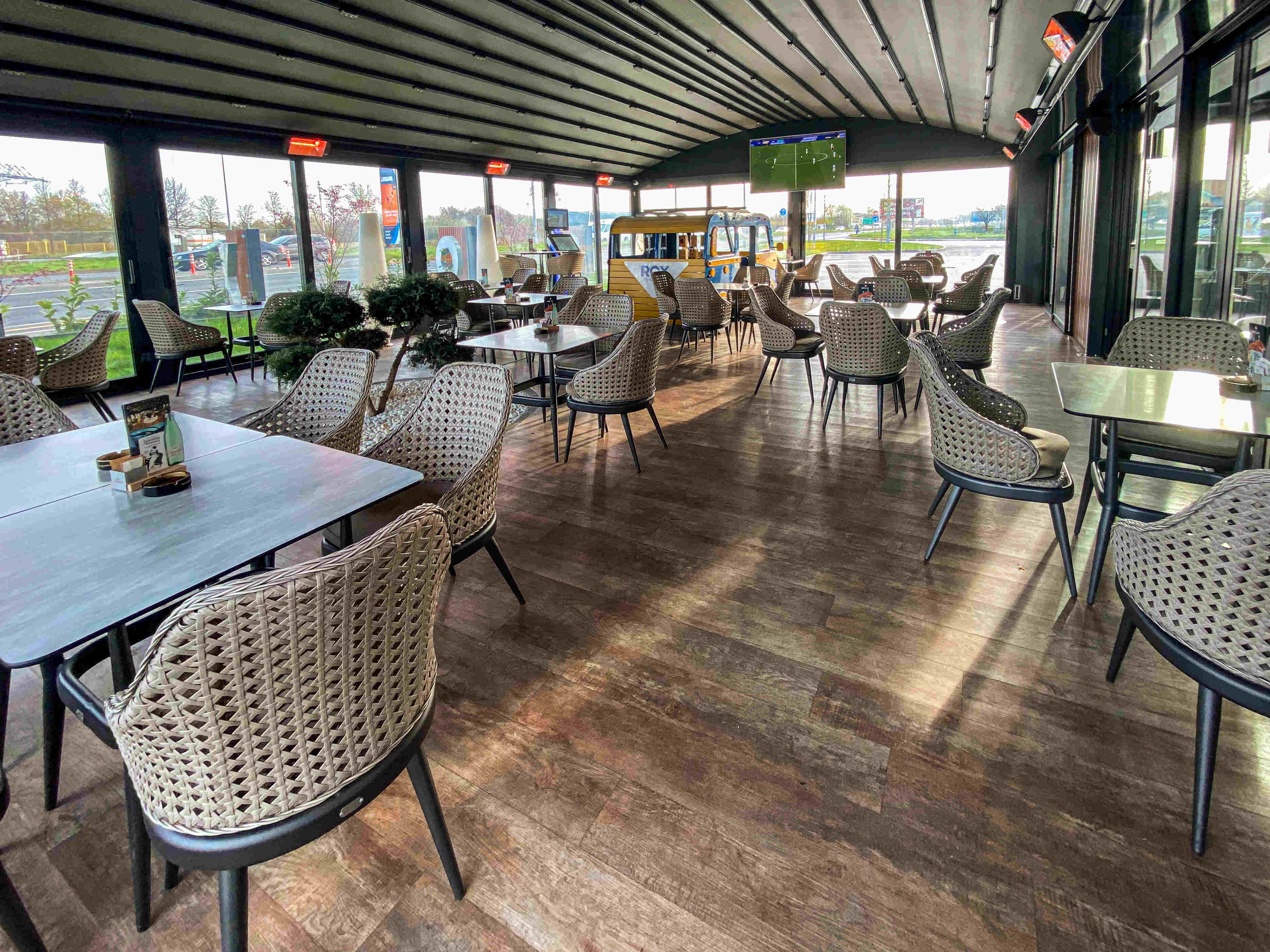 Unutarnja terasa restorana s modernim stolicama, TV ekranom i pogledom na vanjski prostor