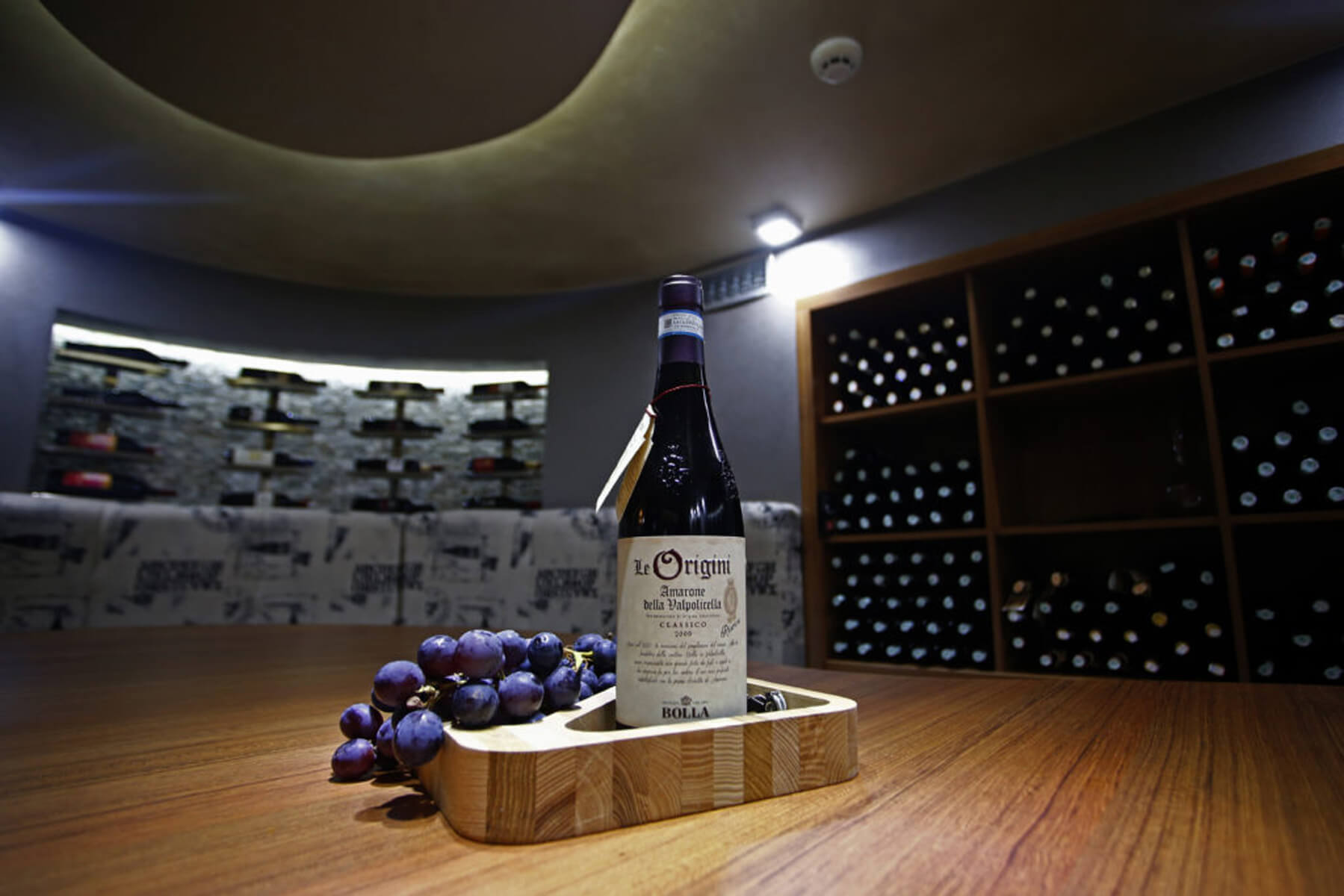 Vino Le Origini s grožđem na drvenom pladnju u vinskom podrumu